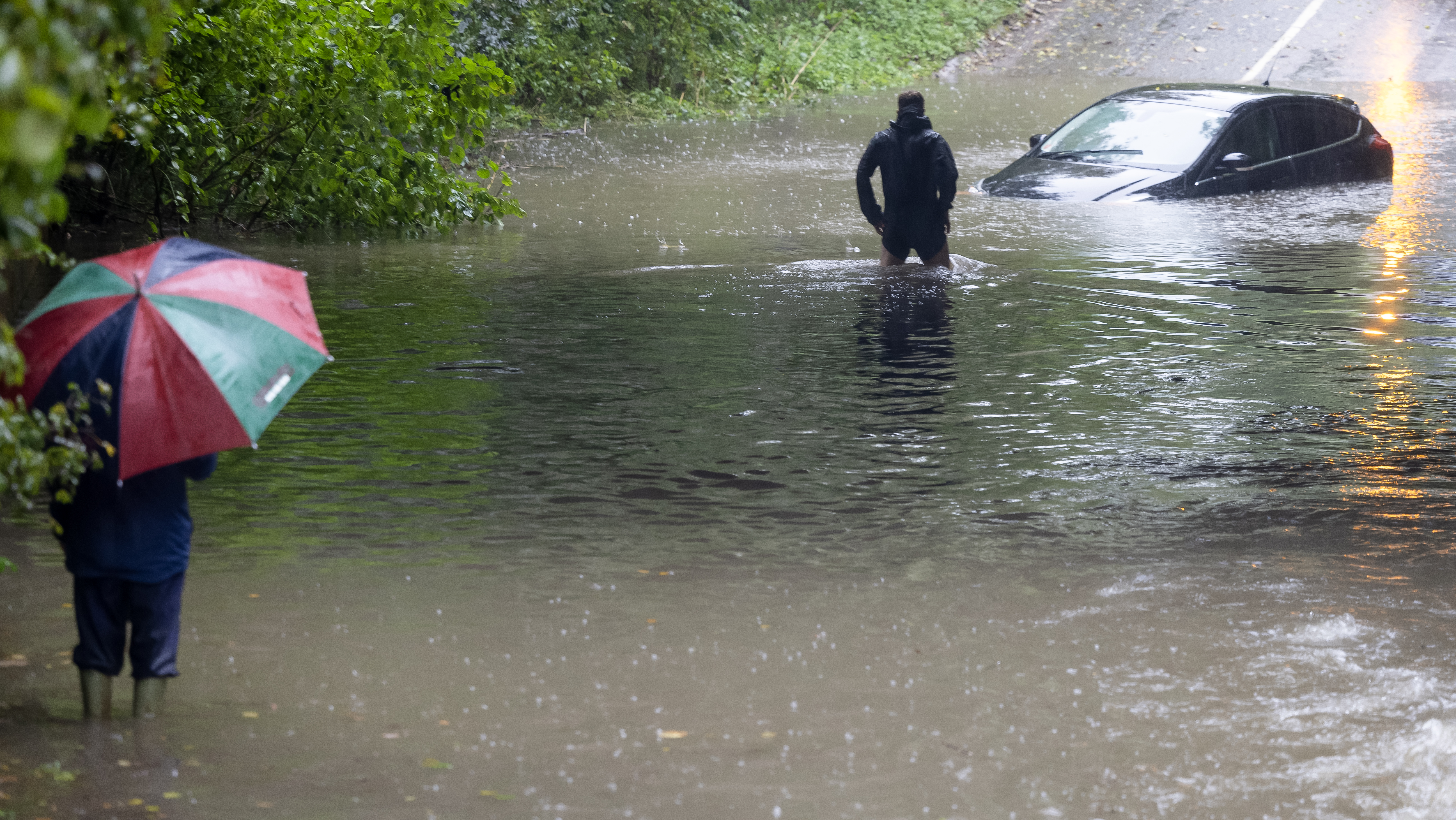 A brave bystander wades in to flood-water in Ashbourne, Derbyshire, to check if anybody is still inside a car stranded in deep water