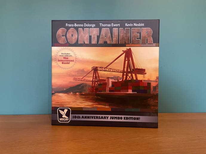 Die Box zum Brettspiel Container (Jumbo Edition), einem Spiel über Containerschiffe.  Es zeigt ein sonnenuntergangsfarbenes Bild eines Containerschiffs, das Fracht aufnimmt.  Funkelnd.
