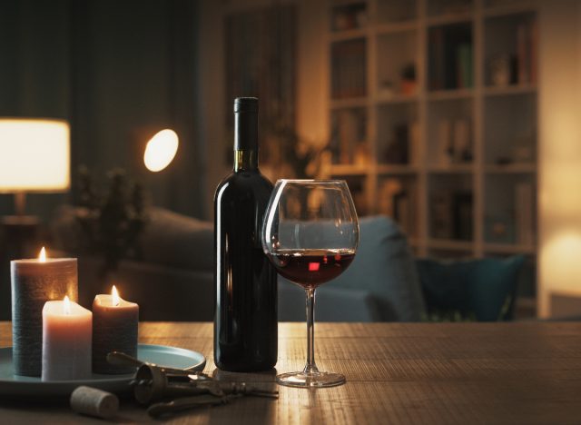 Schlummertrunk, eine Flasche Rotwein und ein Glas auf dem Tisch neben Kerzen