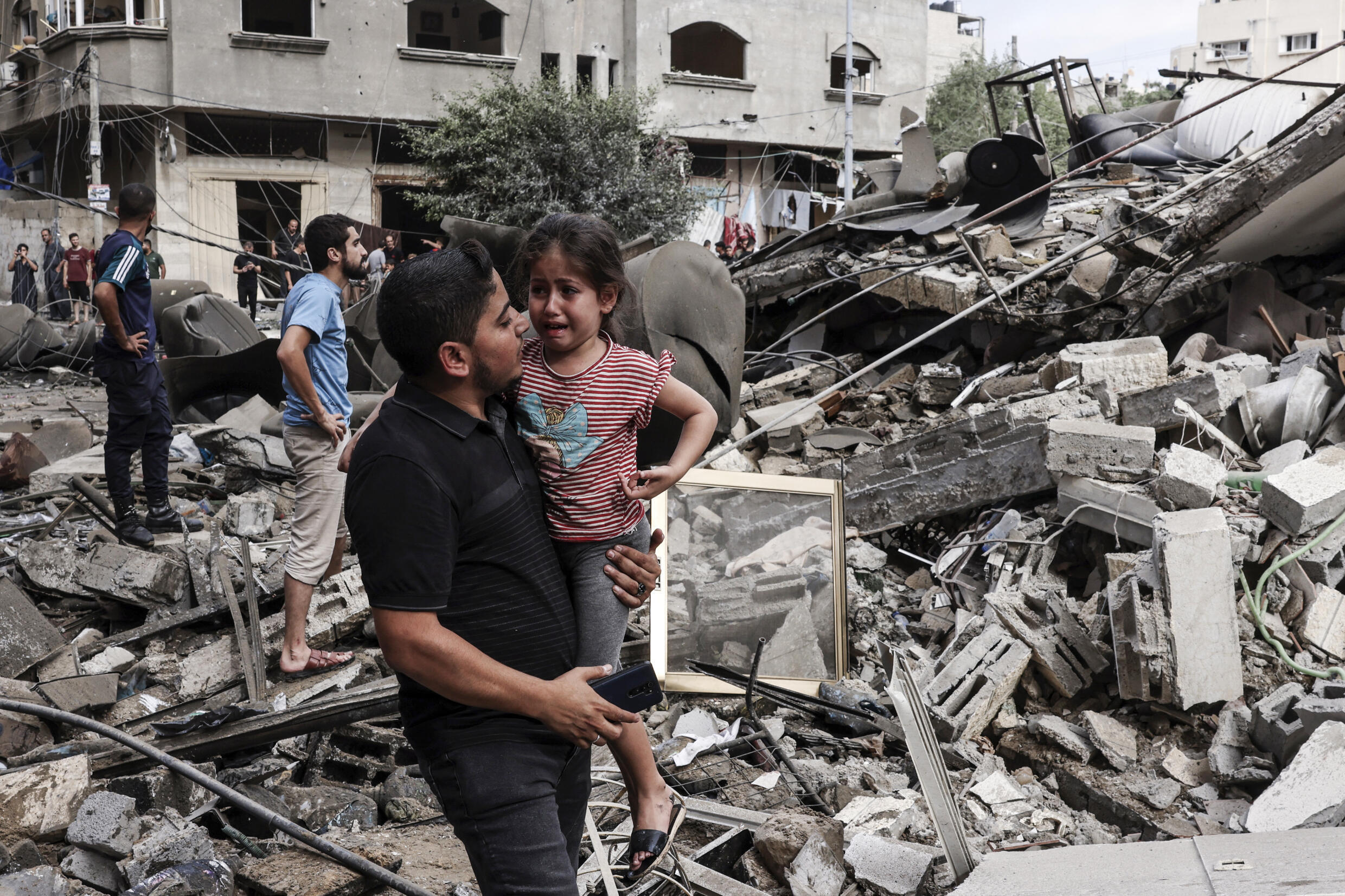 Ein Mann trägt ein weinendes Kind, als er am 7. Oktober 2023 vor einem Gebäude geht, das bei einem israelischen Luftangriff in Gaza-Stadt zerstört wurde.