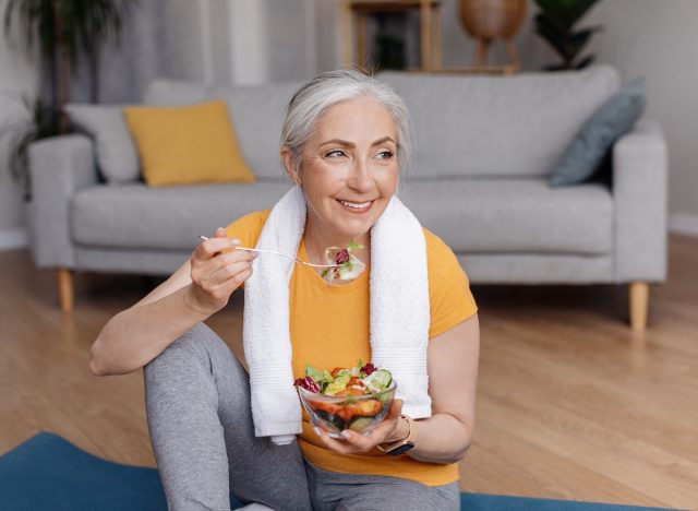 Glückliche, fitte Frau, die Salat auf einer Yogamatte isst, Konzept mit Tipps, um dauerhaft Gewicht zu verlieren