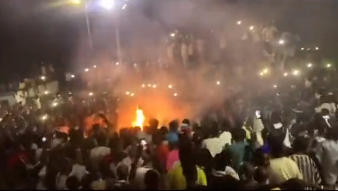 Dies ist ein Screenshot, der die Menschenmenge zeigt, die sich vor dem Feuer versammelt, an dem die Leiche vor dem Friedhof Léona Niassène verbrannt wurde.