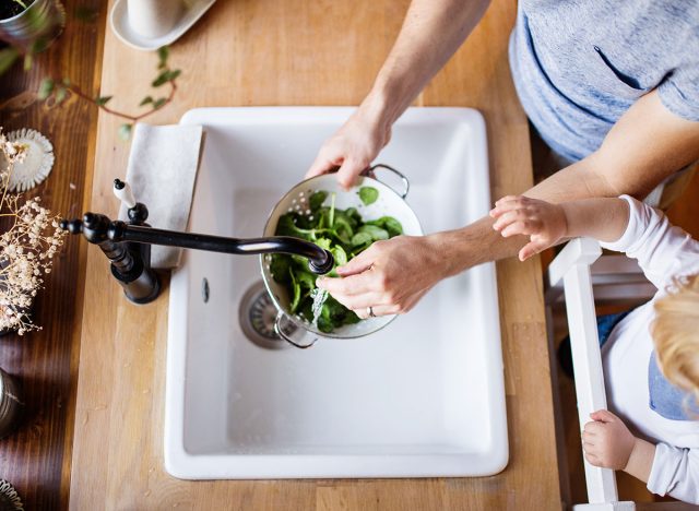 Frau gießt Wasser in Küchenspüle über Salat