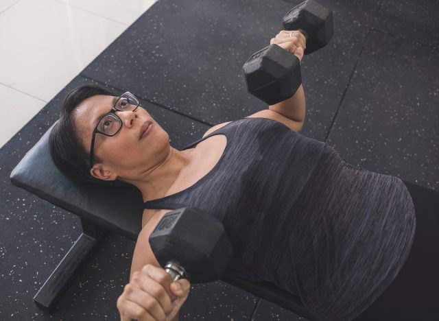 Frau macht auf der Trainingsbank Kurzhantel-Brustpresse-Übungen zur Stärkung des Oberkörpers