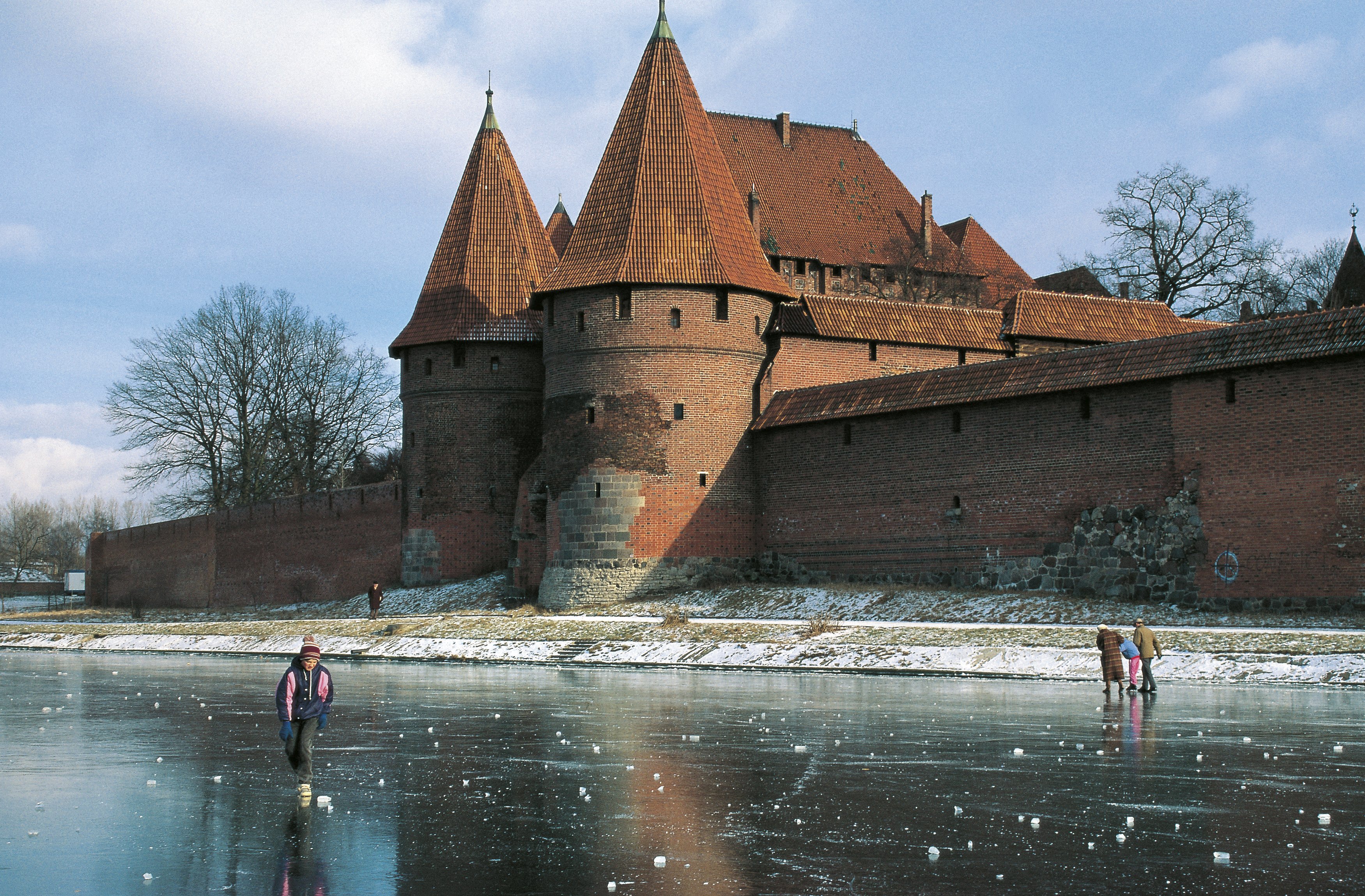 Auf dem zugefrorenen Fluss neben der Burg laufen Menschen Schlittschuh