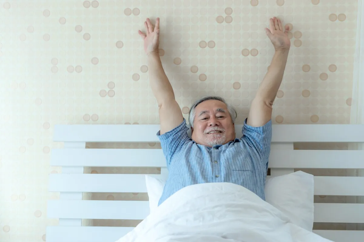 Ein glücklicher älterer Mann mit guter Gesundheit wacht morgens mit Freude in seinem Schlafzimmer auf