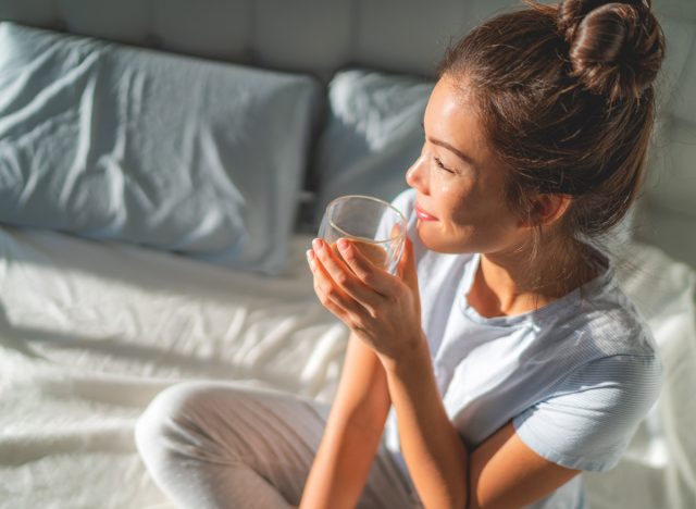 Frau trinkt morgens Tee und Wasser im Bett