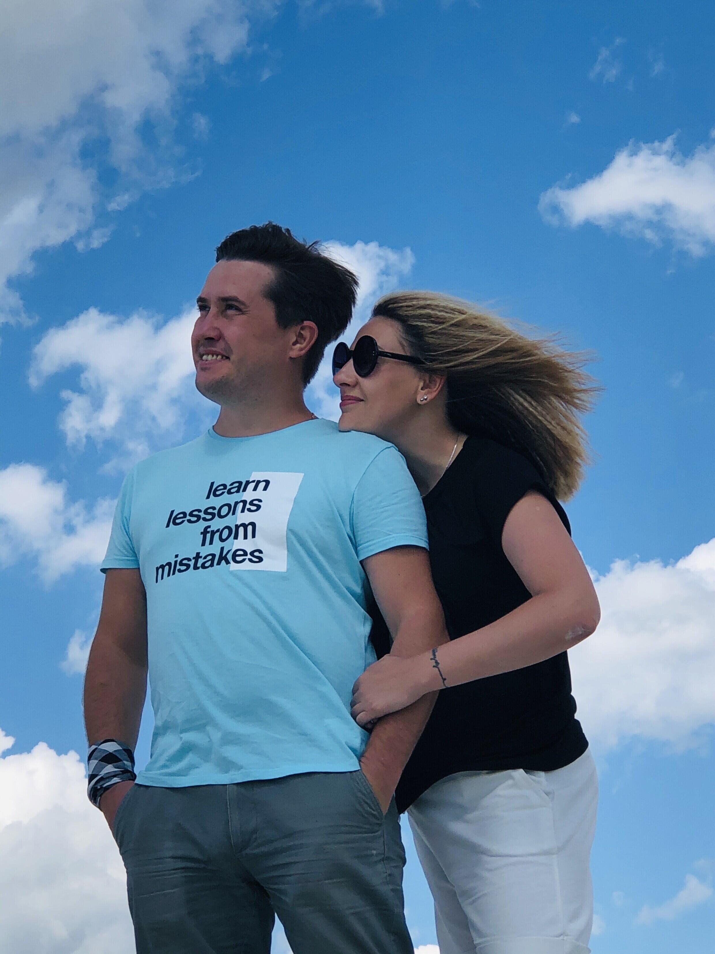 Ein Paar steht zusammen und blickt in die Ferne, hinter sich ein blauer Himmel.