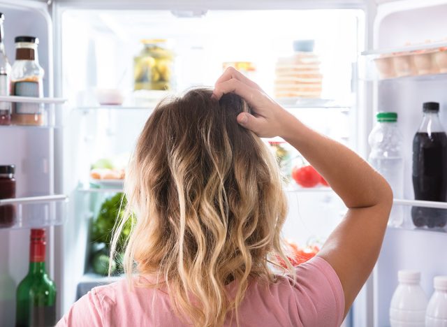 Frau steht hungrig und verwirrt am Kühlschrank