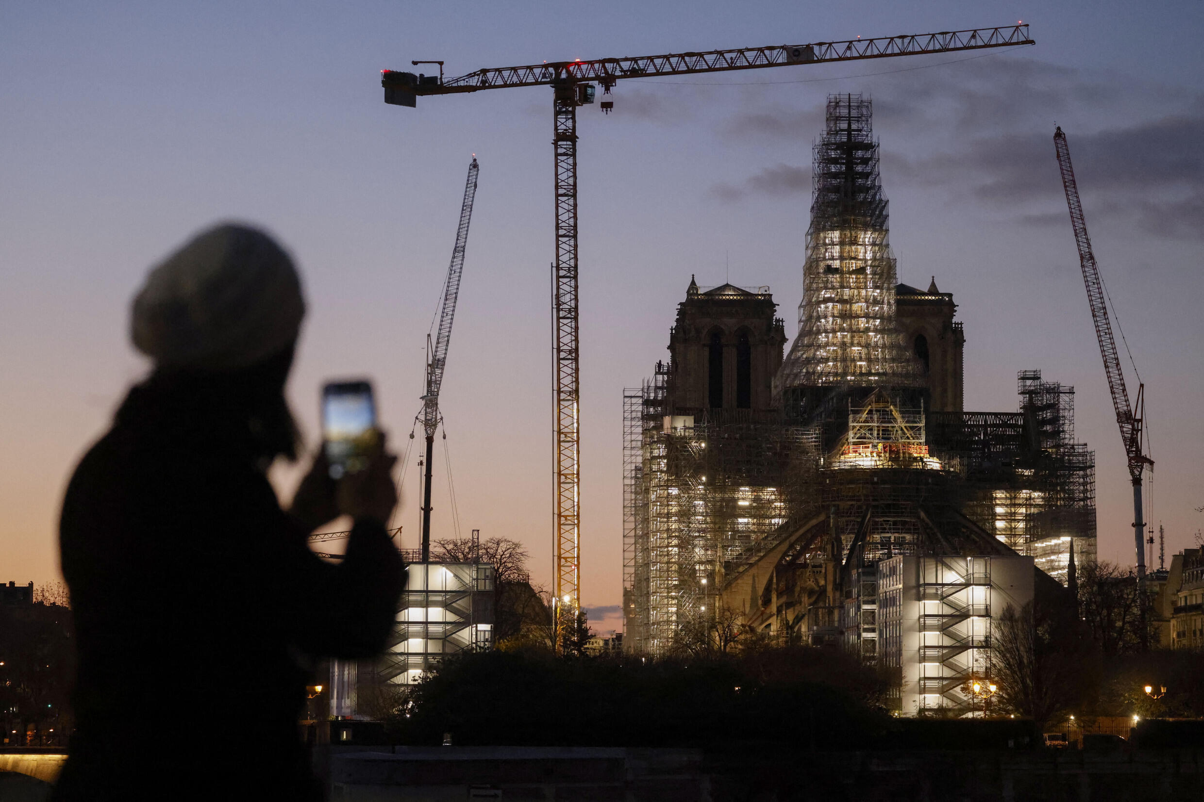Eine Person fotografiert in der Abenddämmerung die Kathedrale Notre-Dame de Paris mit der Holzkonstruktion des neuen Turms, die während der Wiederaufbauarbeiten am 28. November 2020 auf der Ile de la Cite in Paris angebracht war