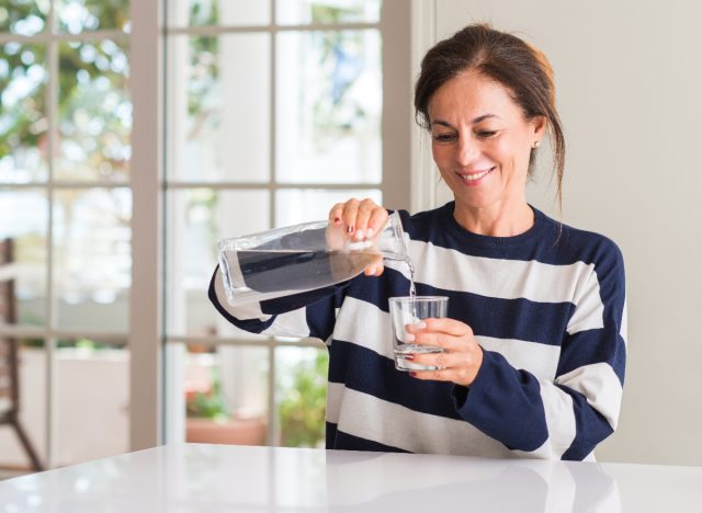 Reife Frau gießt ein Glas Wasser in ihre Küche