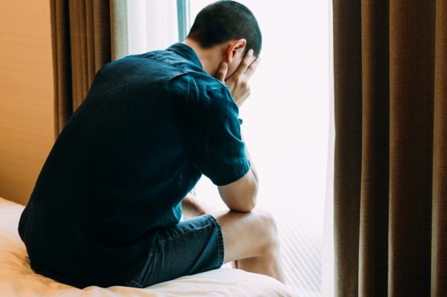 Depressiver Mann mit Problemen sitzt allein, den Kopf in den Händen auf dem Bett und weint