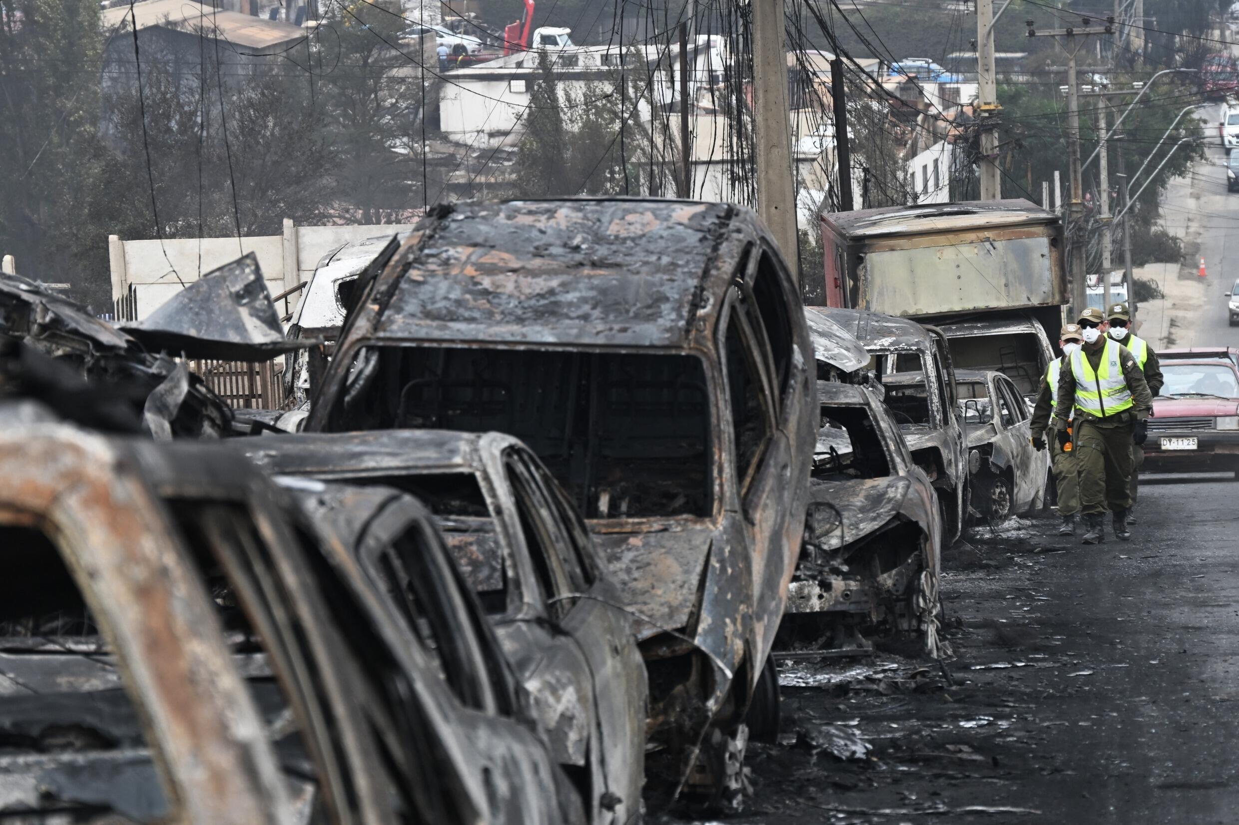 Chilenische „Carabineros“ laufen nach einem Waldbrand in Quilpue, Viña del Mar, Chile, am 4. Februar 2024 an verbrannten Fahrzeugen vorbei.