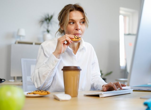 Frau isst Schokoladenkekse und naschen gedankenlos während der Arbeit