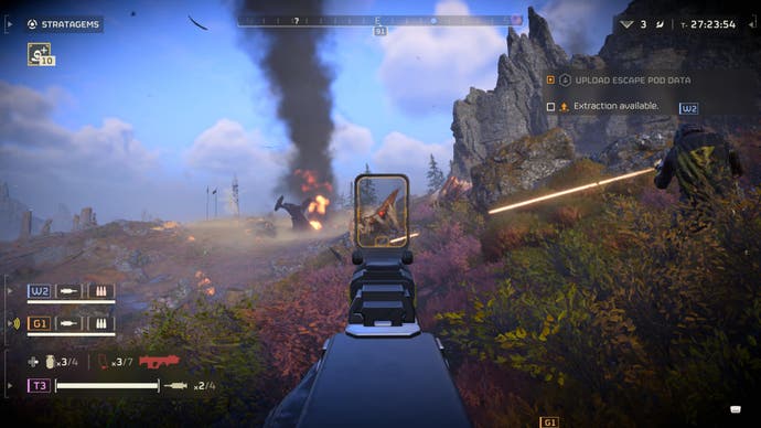 Helldivers 2-Screenshot, der das Gameplay mit Zielen und Visier zeigt, mit einem rauchenden Schiff in der Ferne und Kämpfen um dich herum