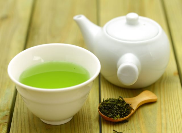 grüner Tee in Tasse und Teekanne und Teeblätter auf Holzlöffel
