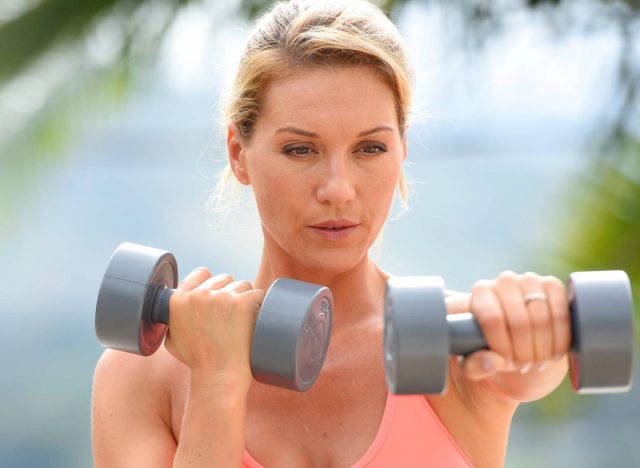 Frau mittleren Alters macht Hantelübungen im Freien, Konzept des Trainings mit freien Gewichten, um Muskelmasse wiederzugewinnen