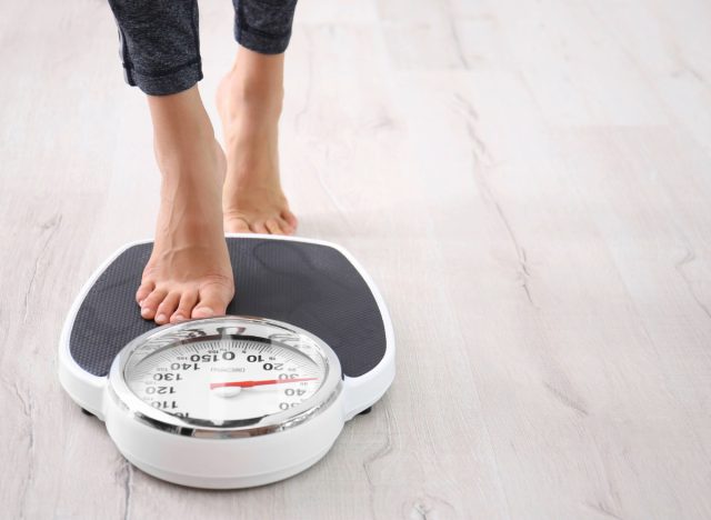 Frau steigt auf die Waage, Konzept, wie viel Gewicht man in einem Monat sicher verlieren kann