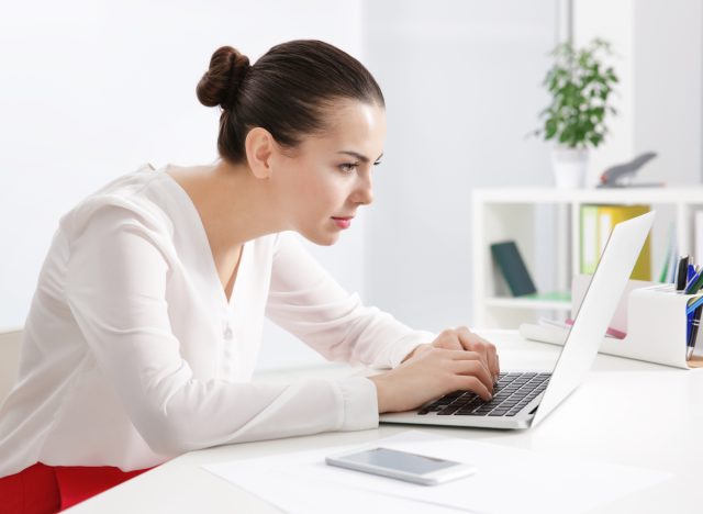 Frau mit falscher Körperhaltung fesselt Laptop am Schreibtisch