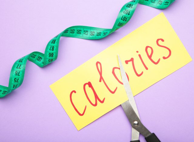 Schere, die gelbes Papier schneidet "Kalorien" Darauf steht das Konzept, wie viele Kalorien man jeden Tag einsparen muss, um Gewicht zu verlieren
