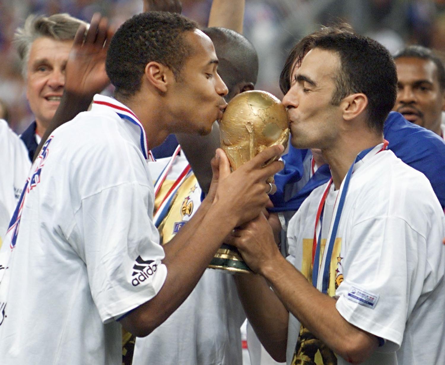 Die französische Fußballlegende Thierry Henry (l.) und Youri Djorkaeff küssen den WM-Pokal, nachdem Frankreich ihn 1998 im Stade de France gewonnen hat.