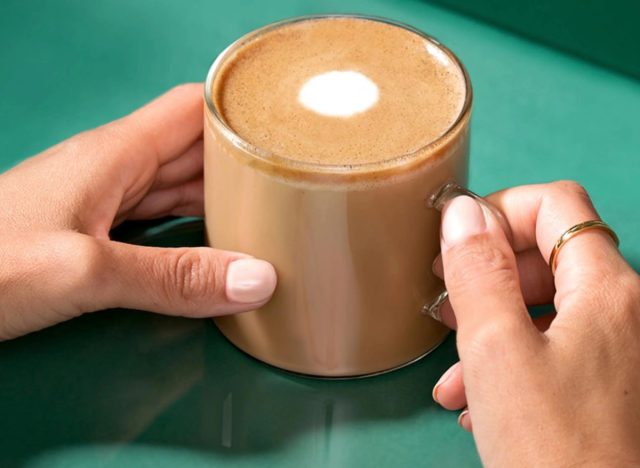 Hände halten einen Becher Starbucks flach weiß auf grünem Hintergrund.