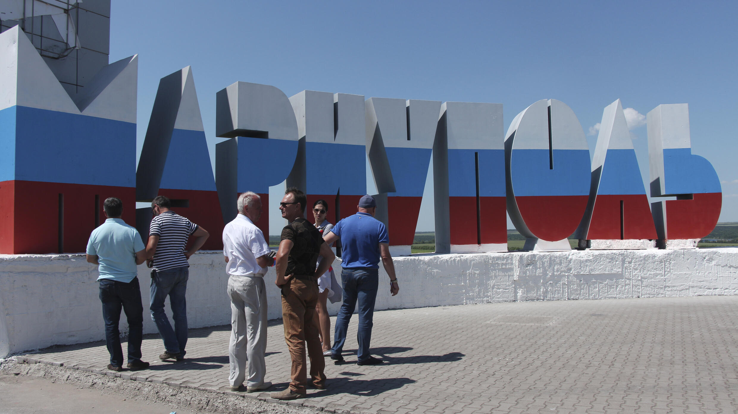 People stand near the sculpture of the name of the city of Mariupol written in Russian and painted in the colours of the Russian national flag during celebration of Russia Day in the city on June 12,