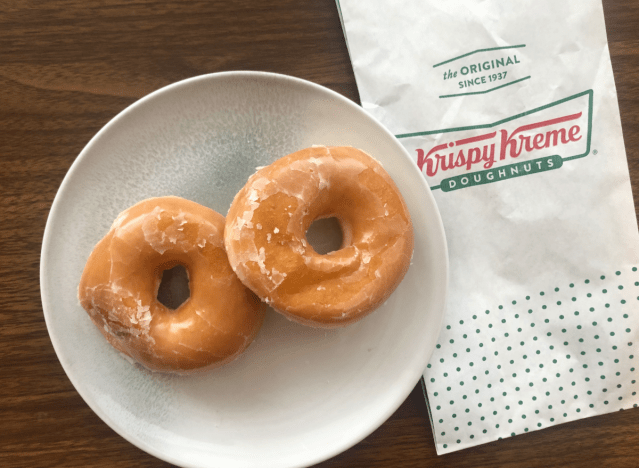 Zwei glasierte Donuts aus Krispy Kreme auf einem Teller mit einer Tüte.