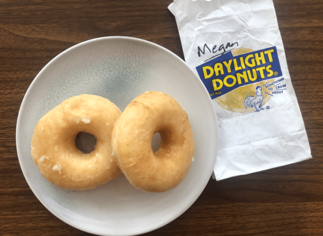 Zwei glasierte Donuts auf einem Teller mit einer Daylight-Donuts-Tüte.
