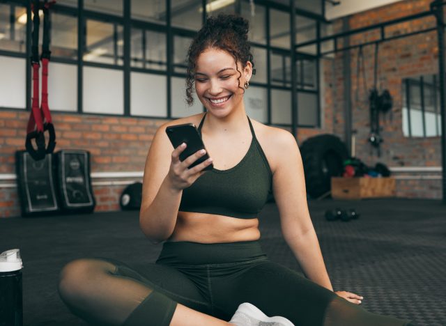 Fitness-Frau auf ihrem Handy im Fitnessstudio Konzept der besten Instagram-Trainer, denen man folgen kann