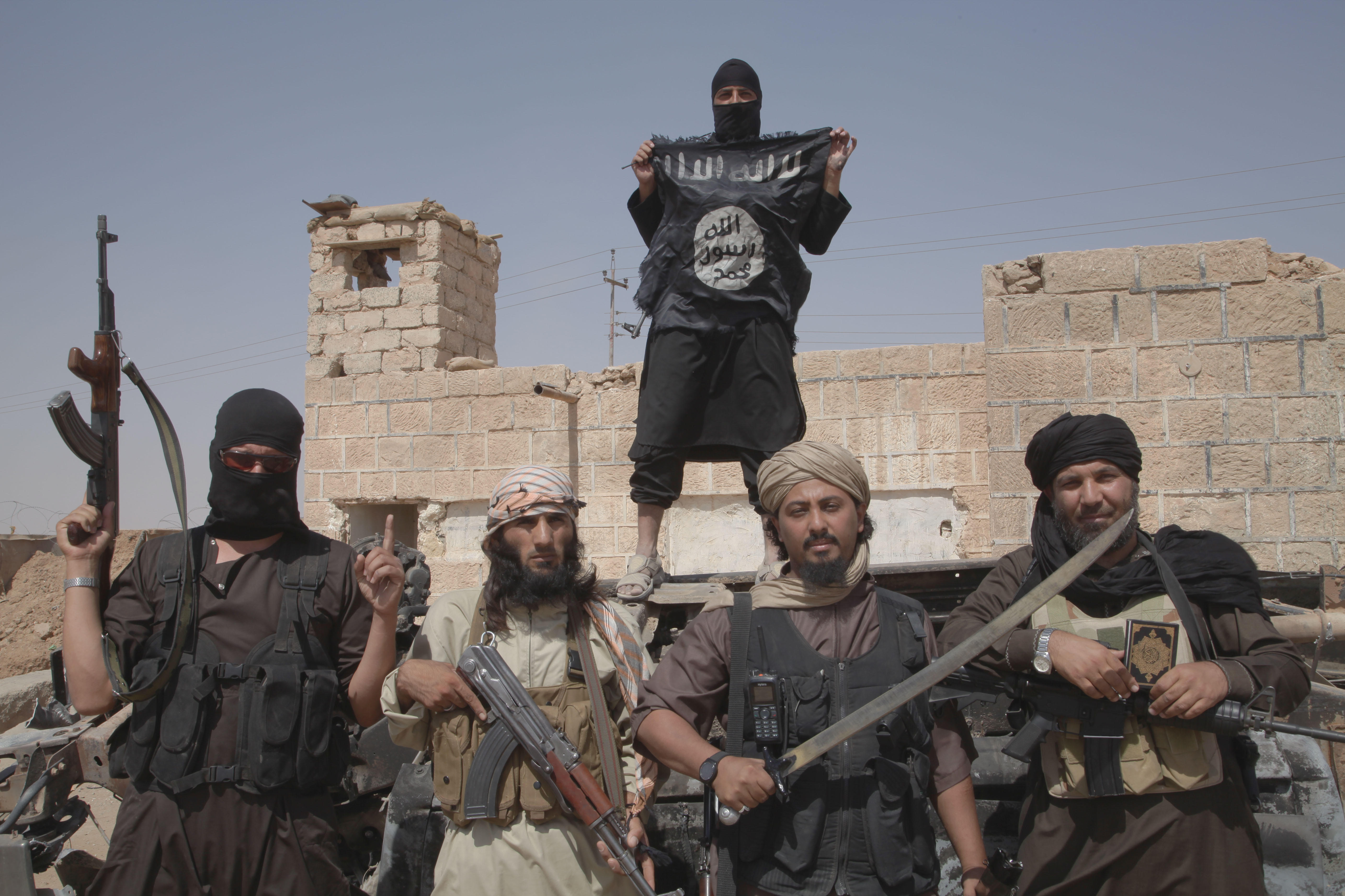 ISIS-Mitglieder schwenken Flaggen, Waffen und Macheten an der Grenze zwischen dem Irak und Syrien